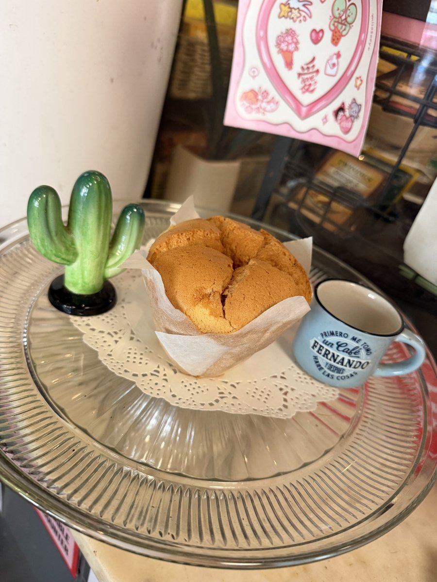 A spongie cake served on a glass cake stand alongside coffee